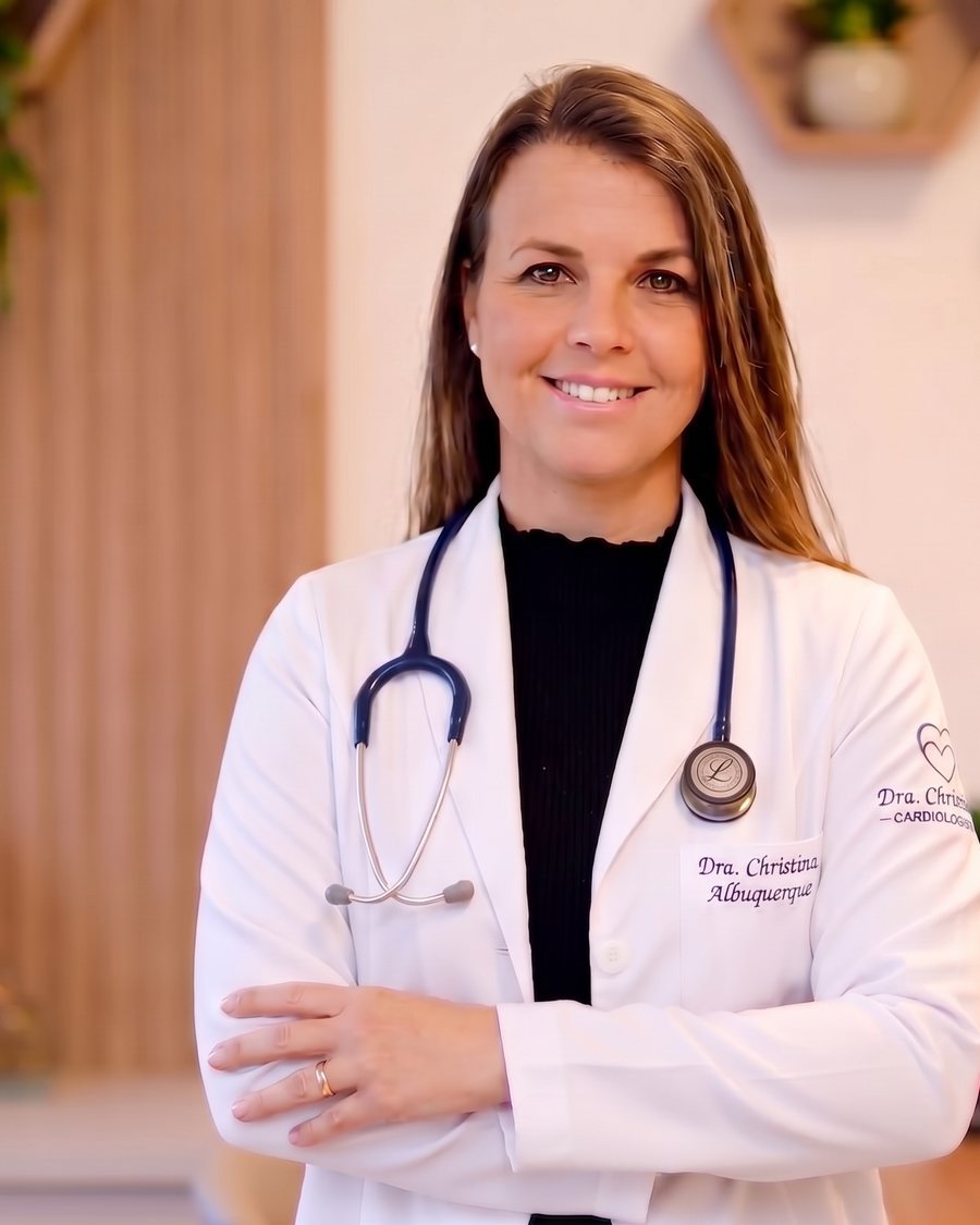 Dra. Christina Albuquerque em seu consultório, de jaleco e estetoscópio